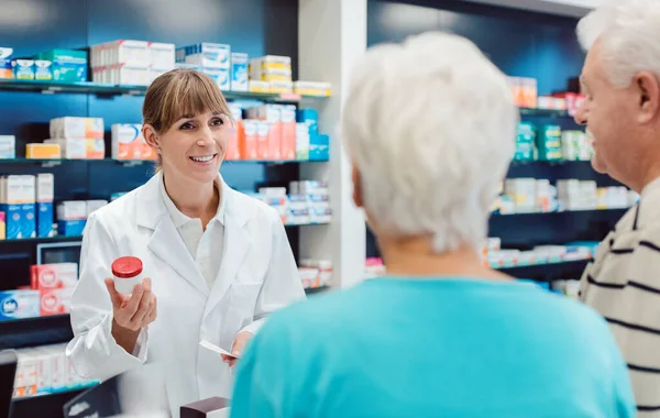 Química asesorando a pareja mayor sobre un medicamento en su farmacia —  Fotos de Stock