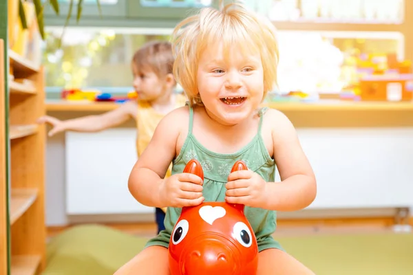 Little girls riding on play horses in kindergarten — Stock Photo, Image