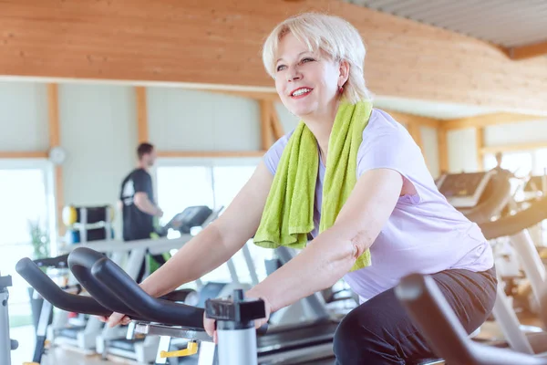 Idős nő gyakorló jobb fitness egy kerékpár a tornateremben — Stock Fotó