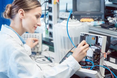 Mühendis kadın test bankında elektronik ürünü ölçüyor.