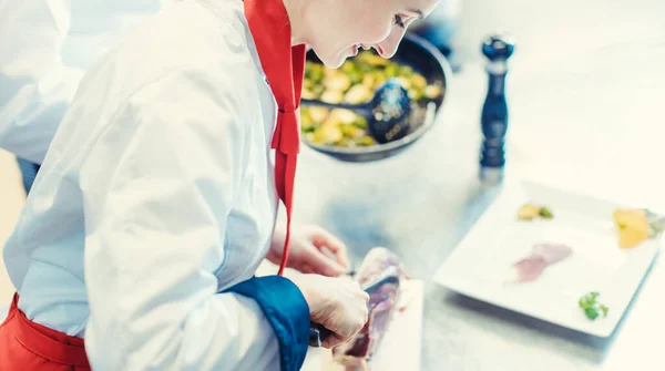 Chef cozinheiro em restaurante chique cozinha fatiar presunto para um prato — Fotografia de Stock