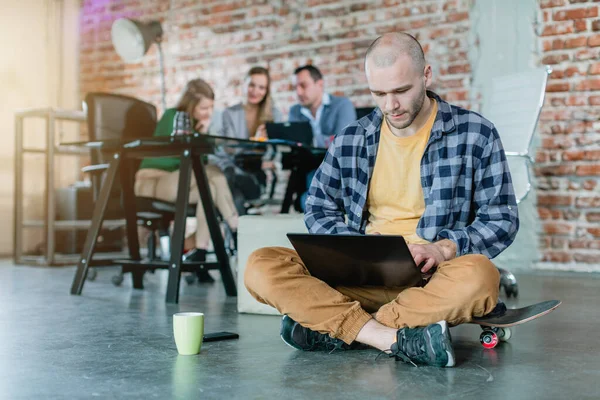 Hip lavoratore in una startup codifica con computer portatile seduto su skateboard — Foto Stock