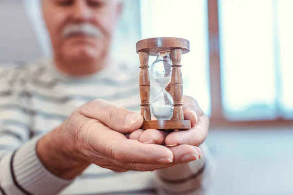 Hombre mayor sosteniendo reloj de arena en casa de retiro, símbolo de vida limitada —  Fotos de Stock