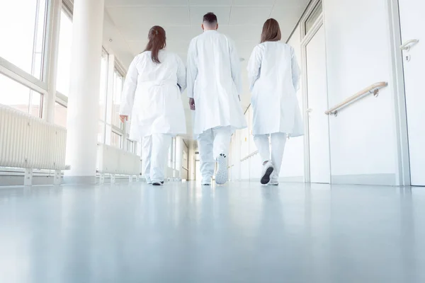 Três médicos a caminhar por um corredor no hospital — Fotografia de Stock