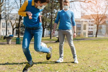 Baba ve oğul Coronavirus krizi sırasında parkta futbol oynuyorlar.