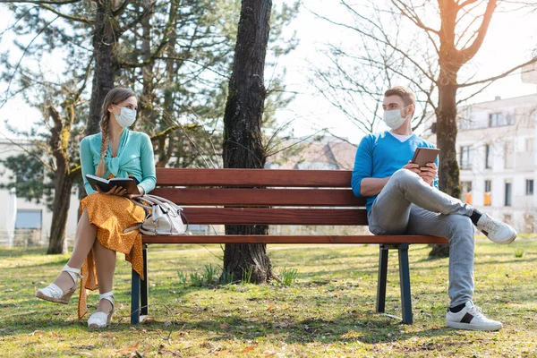 Женщина и мужчина в социальной отстраненности сидят на скамейке — стоковое фото