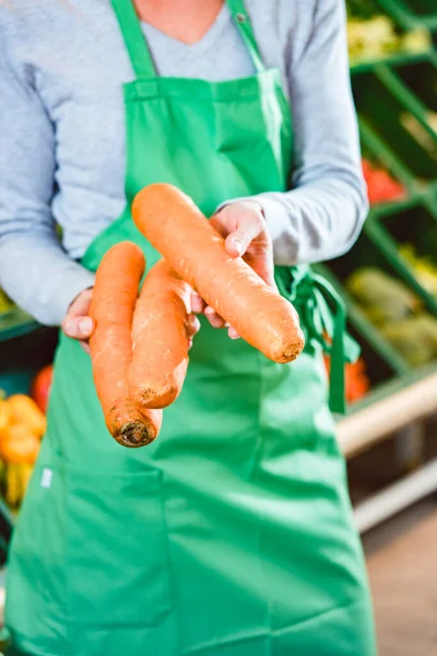 Saleswoman in organic supermarket offering fresh carrots — Stock Photo, Image