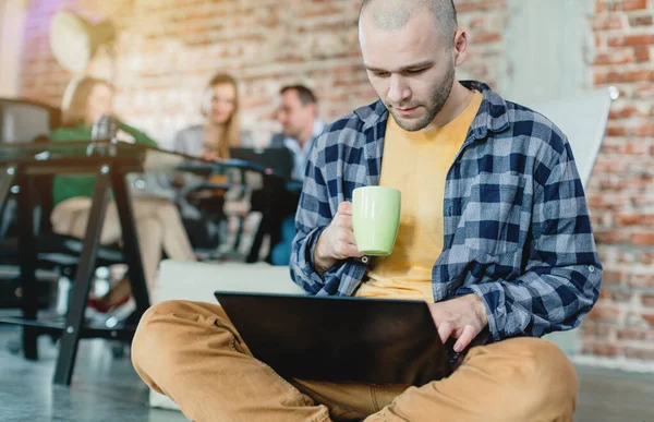 Hip werknemer in een startup codering met laptop zit op skateboard — Stockfoto