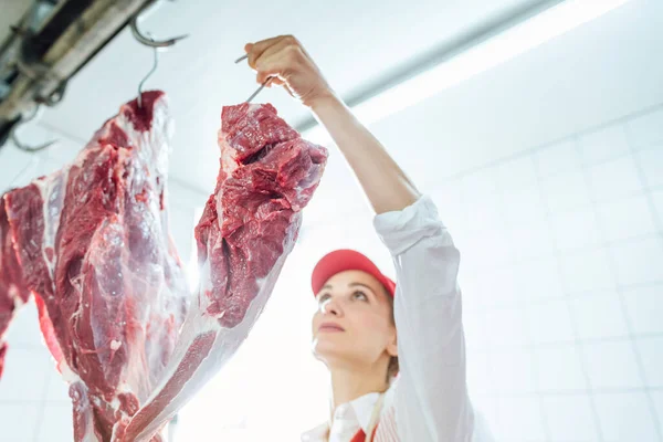 Butcher woman taking meat from hook to cut and sell it — Stock Photo, Image