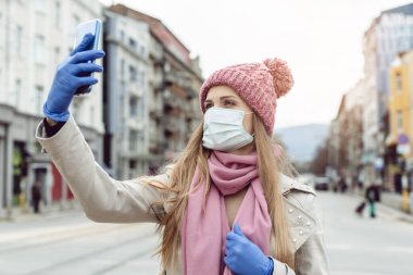 Tıbbi maskeli ve eldivenli bir kadın tecrit şehrinde selfie çekiyor.