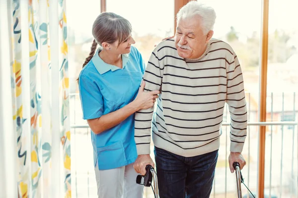 Nurse helping senior man with walking frame in nursing home