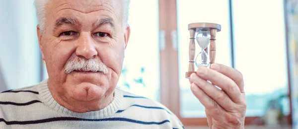 Starší muž držící přesýpací hodiny v domově důchodců, symbol omezeného života — Stock fotografie