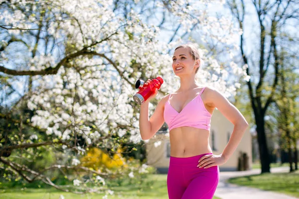 Sportive woman drinking water after sport exercise in park — Stock Photo, Image