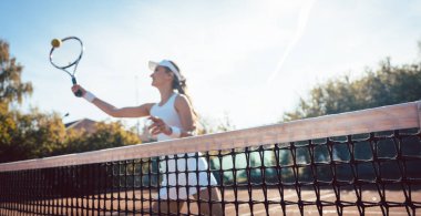 Tenis kortunda top taşıyan bir kadın.