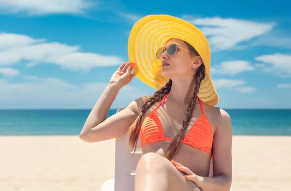 Žena se slunečním kloboukem na lehátku na pláži u moře — Stock fotografie