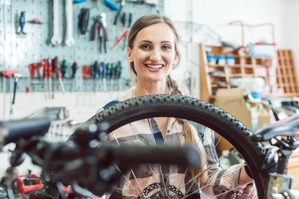 Mujer mecánica de bicicleta mirando a través de la rueda de la bicicleta —  Fotos de Stock