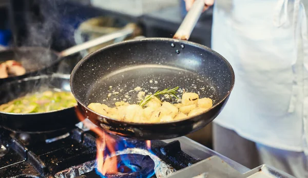 Chef con sartenes en la estufa cocinando en una cocina de restaurante —  Fotos de Stock