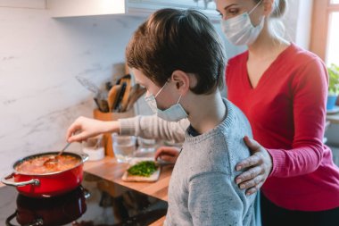 Mother and son cooking at home together wearing masks clipart