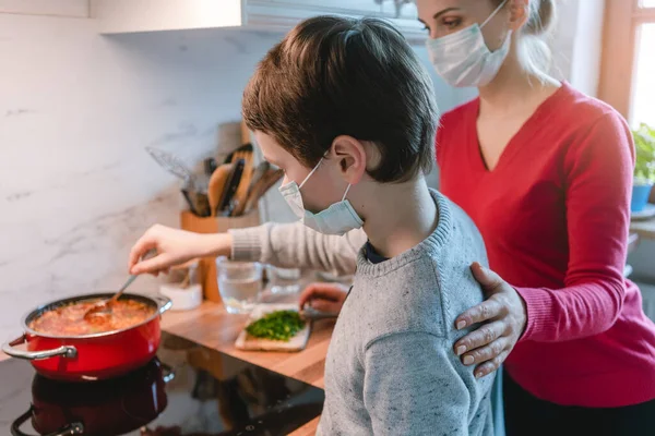 Mother and son cooking at home together wearing masks — Stock Photo, Image