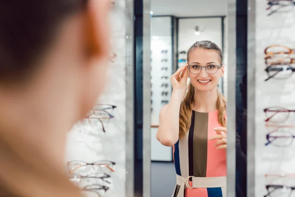 Jovem mulher tentando óculos de moda na loja optometrista — Fotografia de Stock