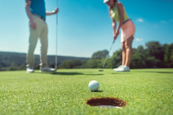 Couple jouant au golf avec la femme sur vert à trou dans — Photo