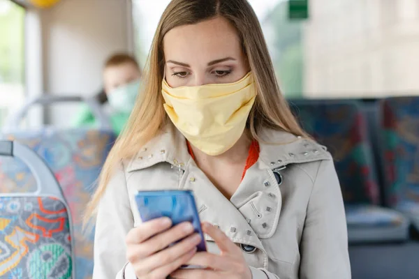 Женщина с телефоном в автобусе в маске для лица — стоковое фото