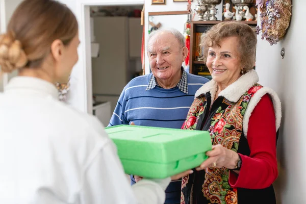 Senior couple greeting volunteer delivering a hot meal to their door — Stock Photo, Image