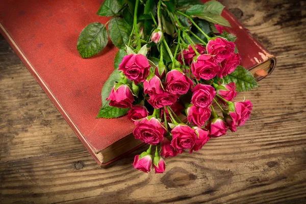 Ροζ τριαντάφυλλα σε παλιό βιβλίο στο ξύλινο τραπέζι — Φωτογραφία Αρχείου