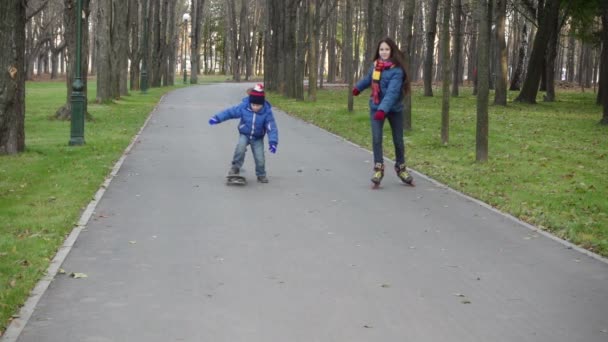 Jongen en meisje rijden in herfst park op rollerblades en scateboard — Stockvideo