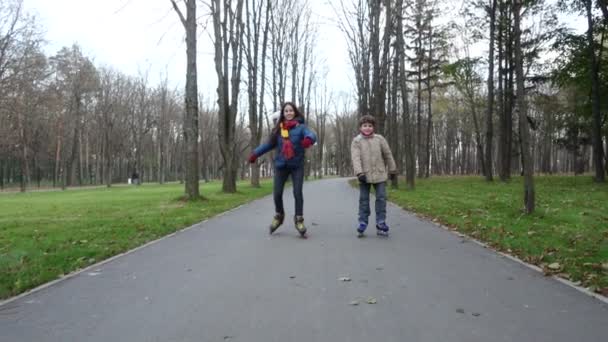 Мальчик и девочка едут в осенний парк на роликах — стоковое видео