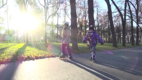 Two little boys ride in autumn park on rollerblades — Stock Video