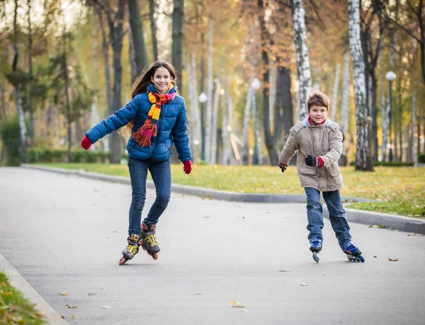 Два счастливых ребенка едут в осенний парк на роликах — стоковое фото