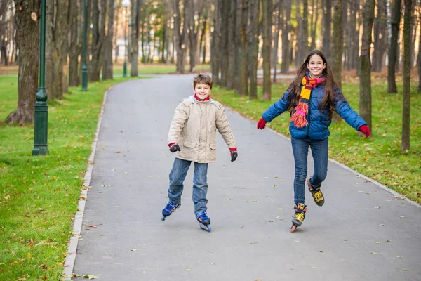 Двое детей едут в осенний парк на роликах — стоковое фото