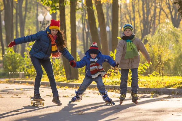 Tre barn lära sig att rida i höst park på rollerblades och s — Stockfoto