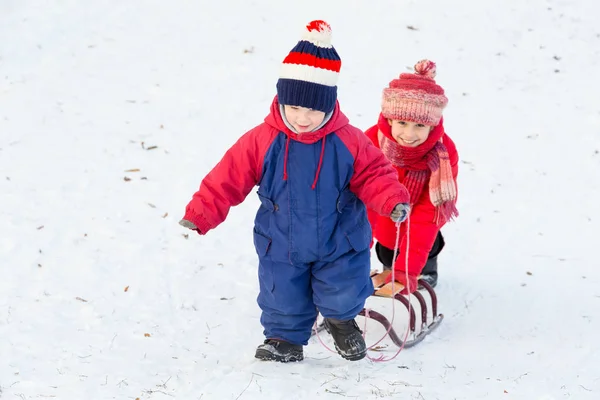 两个孩子快乐与雪橇在雪坡上行走 — 图库照片