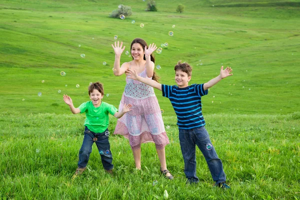 Drei glückliche Kinder fangen die Seifenblasen auf dem Rasen ein — Stockfoto