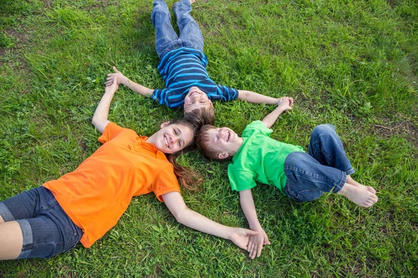 Tres niños felices tumbados sobre hierba verde —  Fotos de Stock