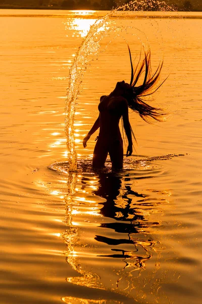 Silhueta de menina na água que espirrando seu cabelo — Fotografia de Stock