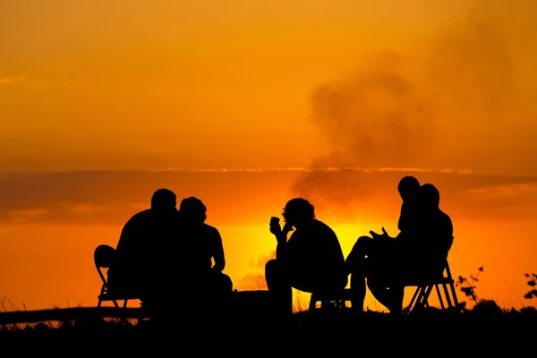 人们在附近反对日落篝火野营坐 — 图库照片