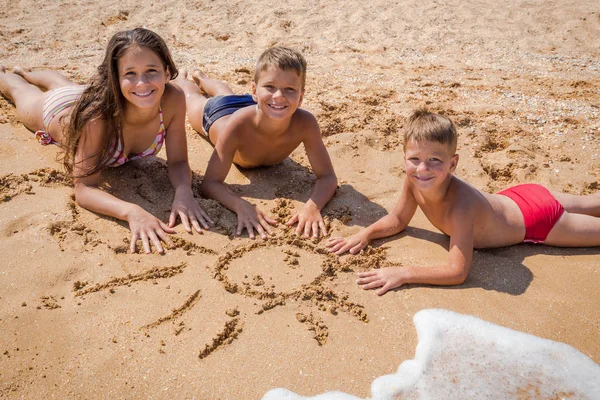 Três crianças deitadas na praia juntas — Fotografia de Stock