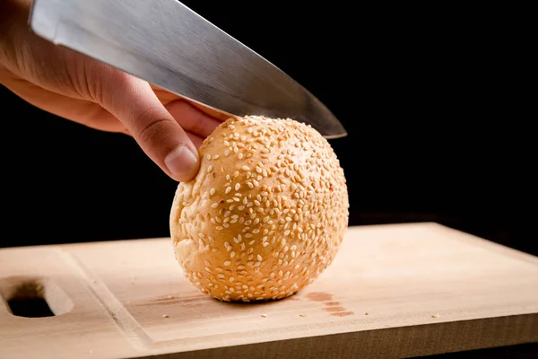 Tagliare i panini con semi di sesamo con un coltello da cucina su legno — Foto Stock