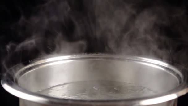 Кип'ятіть воду в металевій сковороді на чорному тлі, повільний рух — стокове відео