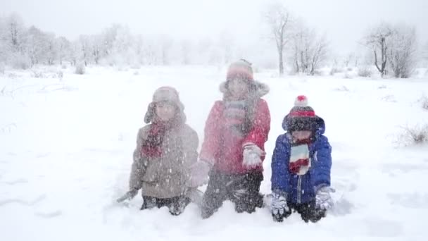 Трое счастливых детей бросают снег в зимний парк, замедленная съемка — стоковое видео