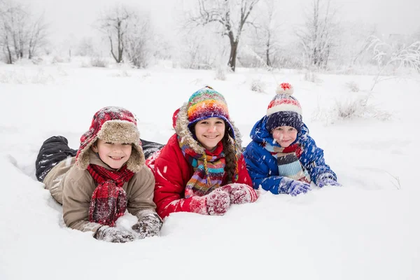 Three kids lying down together on white snow — Stock Photo, Image