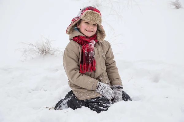 Usměvavý chlapec v teplé oblečení sedí na sněhu — Stock fotografie