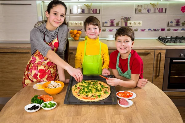 Drie kinderen ingrediënten toe te voegen aan ruwe pizza — Stockfoto