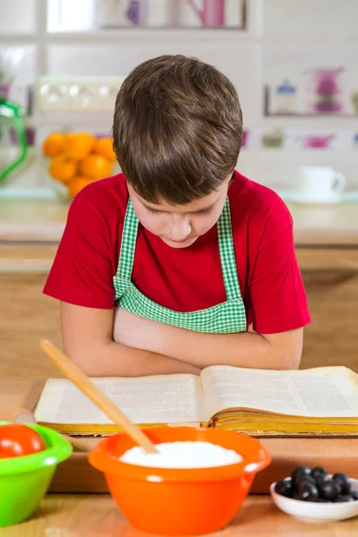 Poika lukee keittokirjaa päivällisen tekoa varten — kuvapankkivalokuva