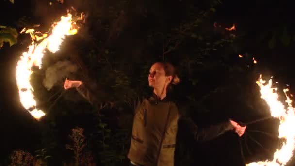 Огненное шоу, девочка вращается пламенем на фоне черных деревьев — стоковое видео