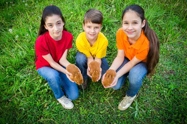 Smiling kids at green grass holding a little rabbits, easter con — Stock Photo, Image