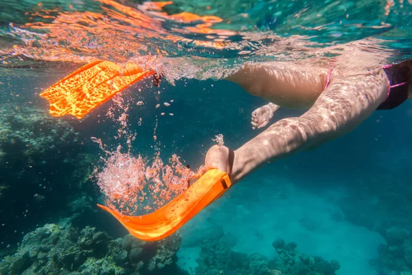 Mädchen Beine in orangefarbenen Flossen unter Wasser im Meer in der Nähe von Korallenriff — Stockfoto